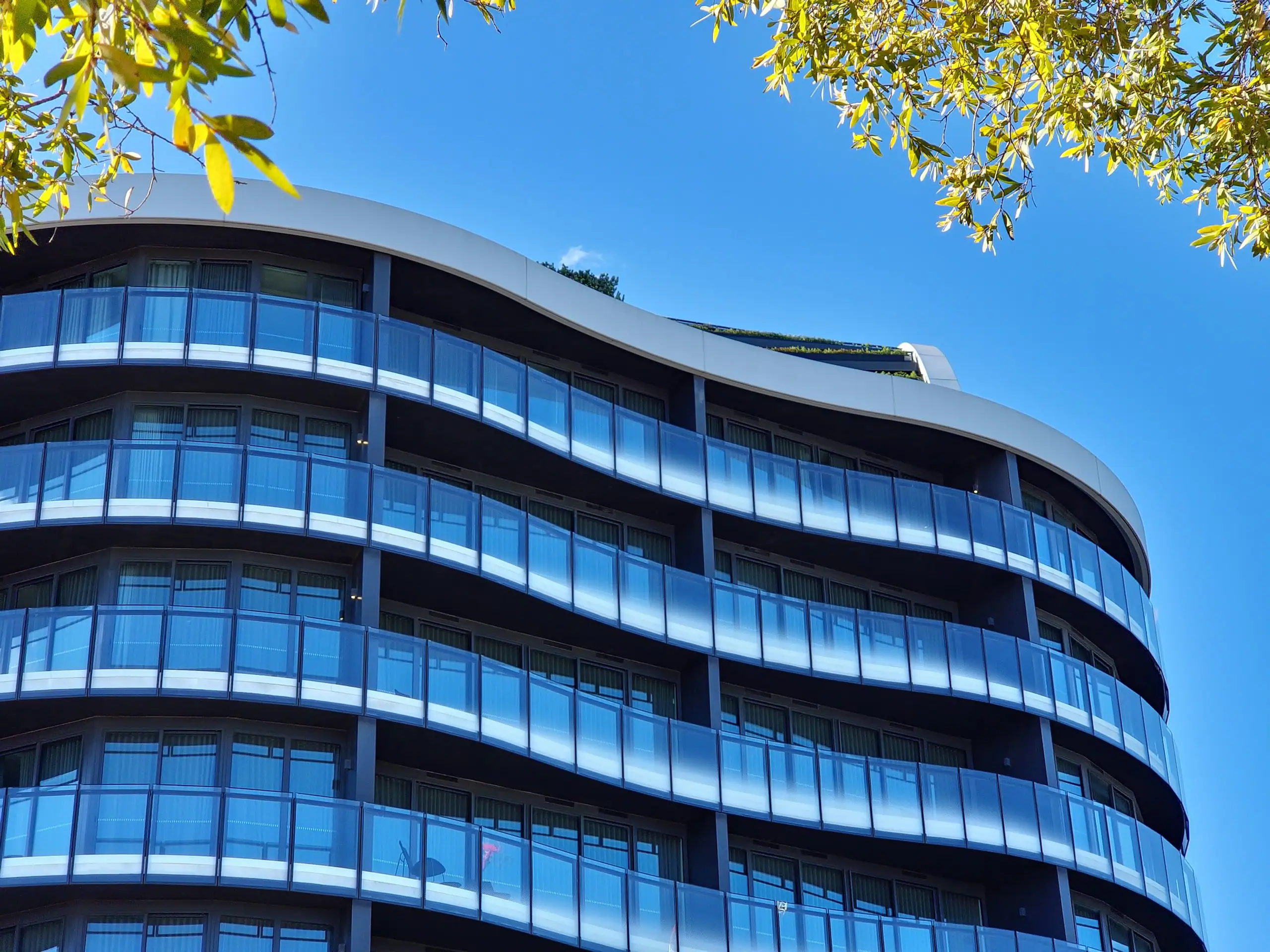 A curved residential tower with glass balustrades on every balcony, against a clear sky